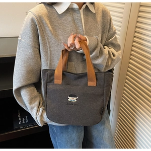 Détail d'un sac en toile anthracite avec poignées brunes et broderie de fille de dessin animé