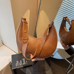Detail of a brown crescent-shaped shoulder bag with smooth leather texture and silver buckle