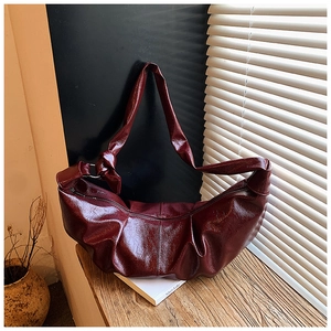 Detailed close-up of dark red pleated crescent bag in glossy leather with textured finish