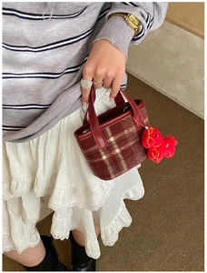 Close-up of a plaid mini handbag with red leather handles and a red plush pony charm