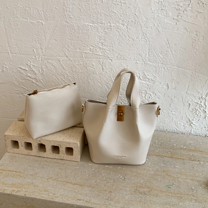 Détail macro du sac seau blanc crème en cuir grainé avec fermoir rotatif doré et pochette