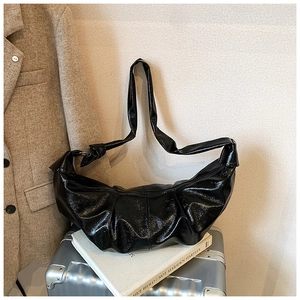 Detail of glossy black hobo bag featuring pleated leather texture and a wide shoulder strap