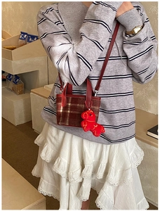 Brown plaid small square crossbody bag with a red plush charm on a model's outfit