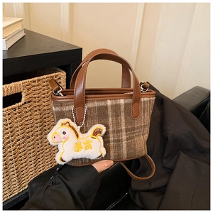 Close-up of brown plaid handbag featuring a white plush horse charm and leather handle
