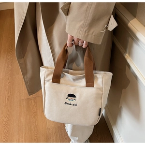 Détail d'un sac cabas en toile crème avec anses brunes et broderie de fille