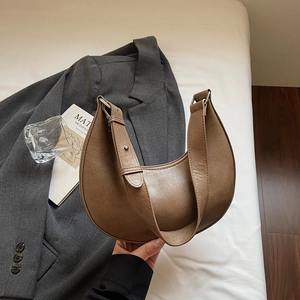 Detail showing the brown crescent shoulder bag held by hand against a suit background