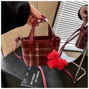 Detail of red-brown checkered wool handbag featuring a plush horse charm and leather strap