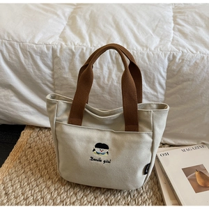Détail du sac cabas en toile avec broderie de fille et poignées en sangle marron