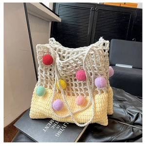 Detailed knit tote bag with colorful pom-poms and cream crochet mesh on black surface