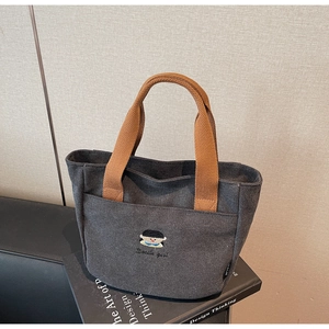 Gros plan du sac en toile gris foncé avec broderie cartoon et poignées tressées