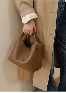 Detalle de bolso tipo cubo de cuero marrón oscuro con gabardina de color caqui clásico