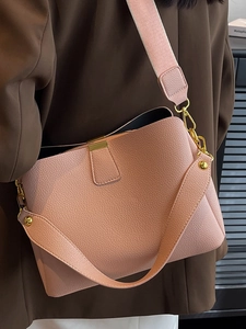 Pink pebbled leather bucket bag with wide woven strap and gold hardware worn with a suit