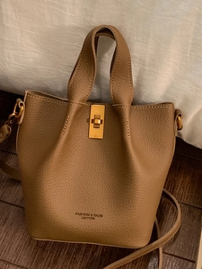 Sac seau en cuir marron avec boucle dorée et bandoulière réglable sur parquet en bois