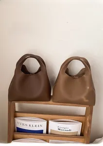 Bolsos bowling chic en cuero marrón y beige sobre un revistero de madera de estilo minimalista