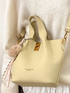 Sac seau en cuir crème chic avec fermoir doré et breloque pompon sur mannequin femme