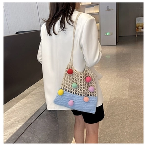 Detail of knit tote bag with colorful pom-poms and blue woven base on a model's shoulder