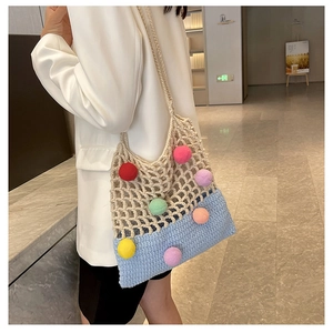 Detail of hand-crocheted shoulder bag with colorful pom-poms and hollow mesh texture