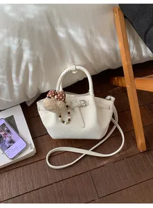 Detail of white bucket bag featuring silver buckle, plush dog charm, and pearl strap