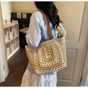 Close-up of a hand-woven straw tote bag featuring brown leather straps and a yellow tulip accent