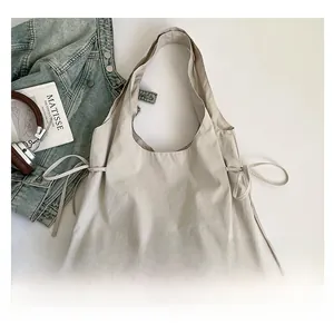 Detail der beigen Nylon-Einkaufstasche mit Kordelzug und gewebtem Etikett auf Denim-Hintergrund
