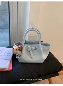 Detail of light blue bucket bag featuring decorative strap and cute plush bear charm