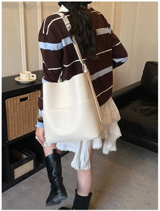 Close-up of a cream-colored leather bucket bag with a wide shoulder strap and lychee texture