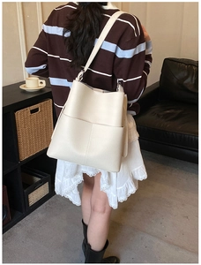 Detail of a creamy white pebbled leather bucket bag with a front pocket and adjustable strap