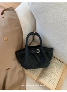 Detail of black matte bucket bag with silver metal buckles on a textured sofa