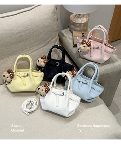 Five small bucket bags in assorted colors with teddy bear charms on a sofa