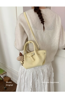 Detail view of cream bucket bag with pleated texture and cute pom-pom charm decoration