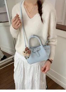 Detail of light blue bucket bag with cute bear charm and bow tie on white knit dress