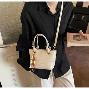Dettaglio della borsa a secchiello bianco crema con nappa in legno e logo marchio
