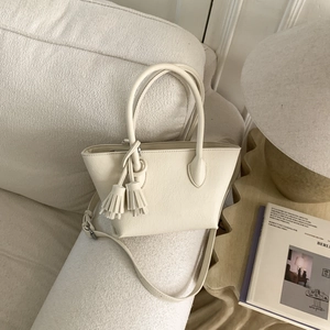 Détail du sac seau blanc crème avec texture en cuir grainé et pendentifs à pompons