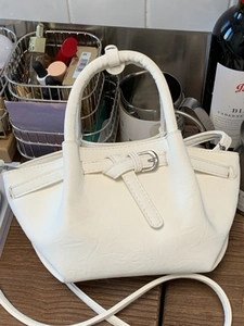 White bucket bag with knot detail and silver buckle on a dark wooden surface
