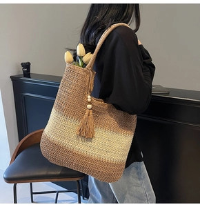 Detail of a large gradient straw tote bag with tassel charm held by a model