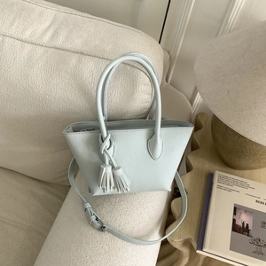 Détail du sac seau vert menthe clair avec pampille posé sur un canapé doux