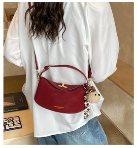 Detail of burgundy half-moon crossbody bag with plush bear pendant and gold buckle closure