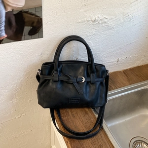 Detailed close-up of soft black leather tote with pleated design and metallic strap buckle