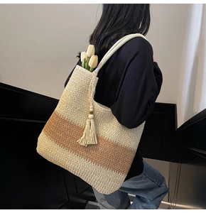 Detail of woven straw tote bag featuring color-block stripes and a tassel with wooden beads