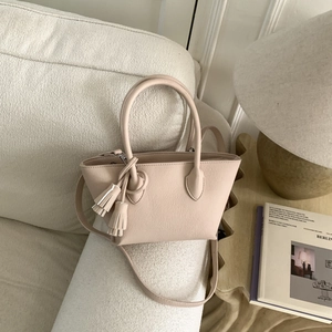 Détail du sac seau beige clair montrant la texture litchi et un pompon élégant