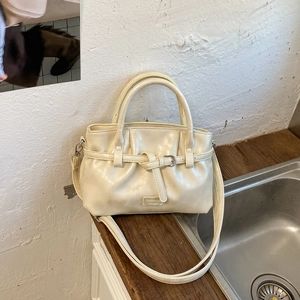 Detail of cream bucket bag showing double handles, metal buckle strap and brand logo