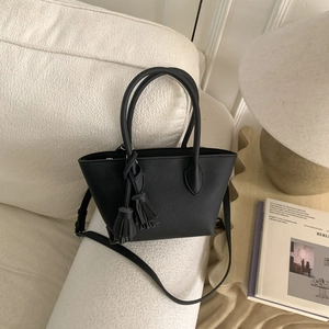 Vue détaillée d'un sac seau en similicuir noir avec pompons sur un canapé blanc