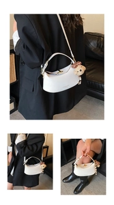 Detailed view of white crescent shoulder bag with golden clasp and cute bear charm pendant