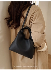 Detalle de un bolso tipo cubo en cuero negro combinado con una gabardina beige