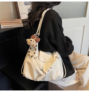 Off-white leather tote bag shown on shoulder featuring cute plush bear charm and front pocket