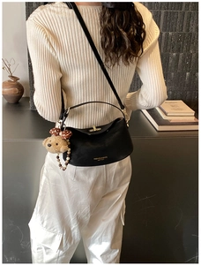 Close-up of black leather crossbody bag with gold buckle and plush bear charm detail