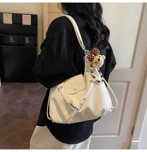 Detail view of cream white half-moon shoulder bag with cute teddy bear charm and silver hardware