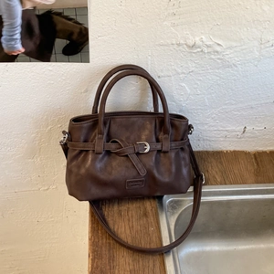 Detail view of coffee brown textured faux leather handbag with shoulder strap and metal buckle