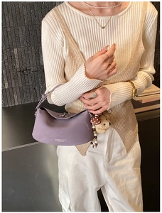 Close-up of a purple half-moon leather shoulder bag with bear charm and pearl accessories