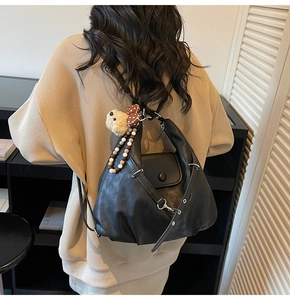 Detail of black leather backpack with plush bear charm and colorful bead straps on model